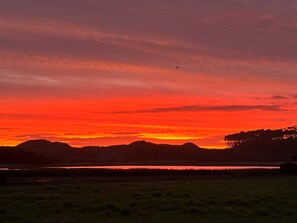 A sunset over a landscape with a body of water, hills, and a clear sky.