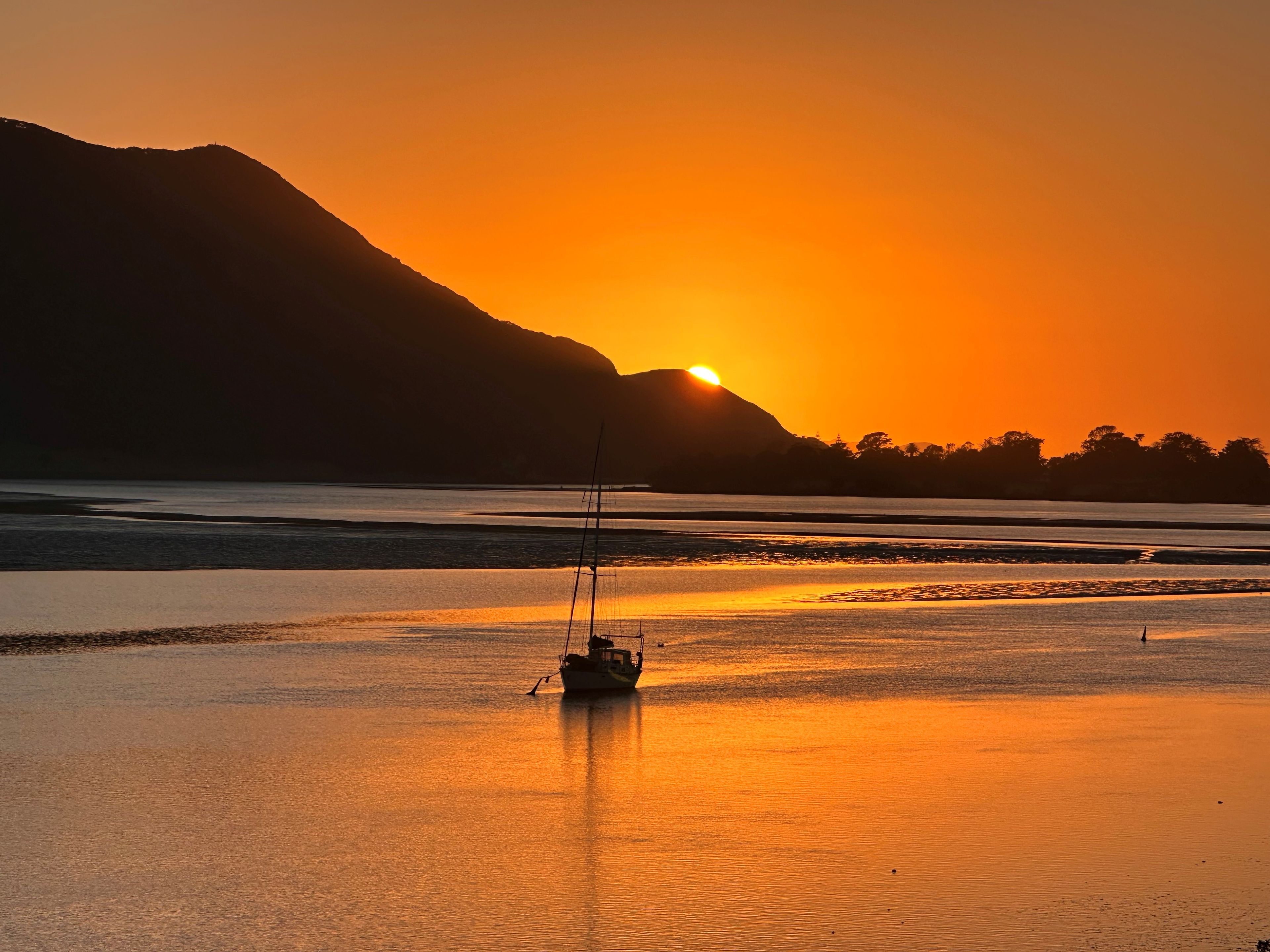 Ein Boot auf ruhigem Wasser bei Sonnenuntergang, im Hintergrund ein Berg.