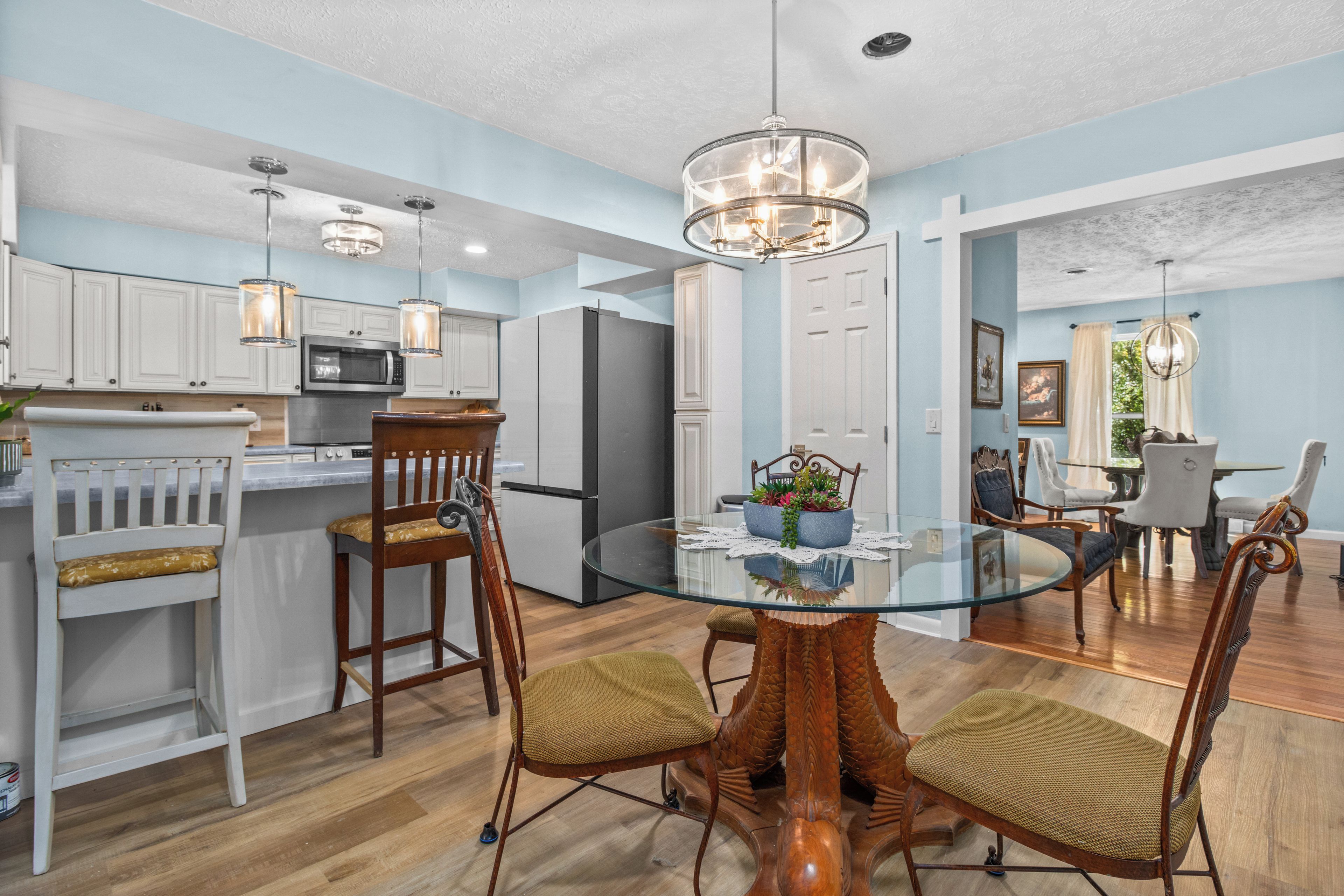 A modern kitchen with white cabinets, a stainless steel refrigerator, and a dining area with a glass table and wooden chairs.