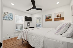 Ein Schlafzimmer mit einem Bett, einem Deckenventilator, einem Fernseher und Kunstwerken an den Wänden.