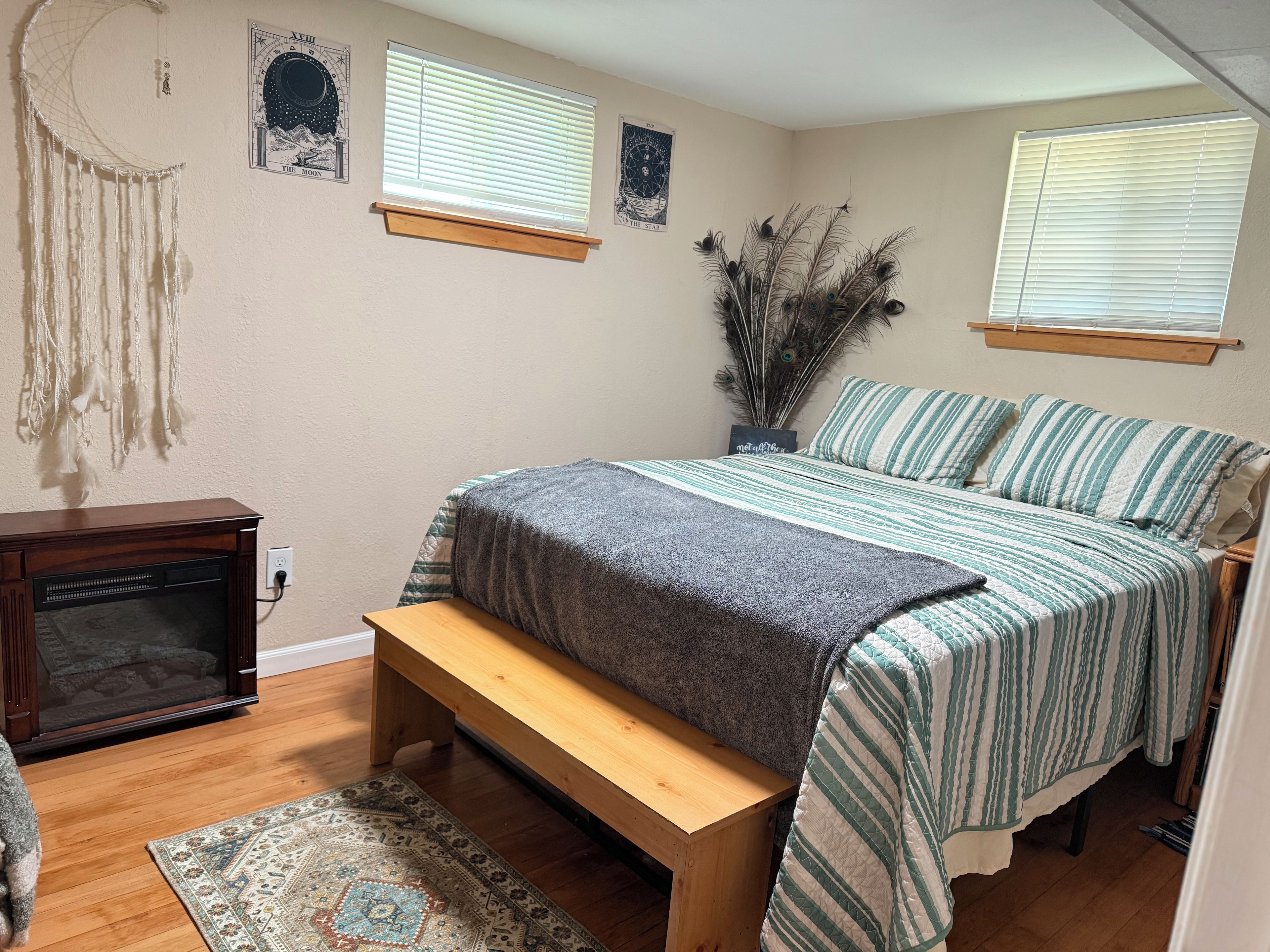 A bedroom with a bed, bench, wall art, and a decorative plant.