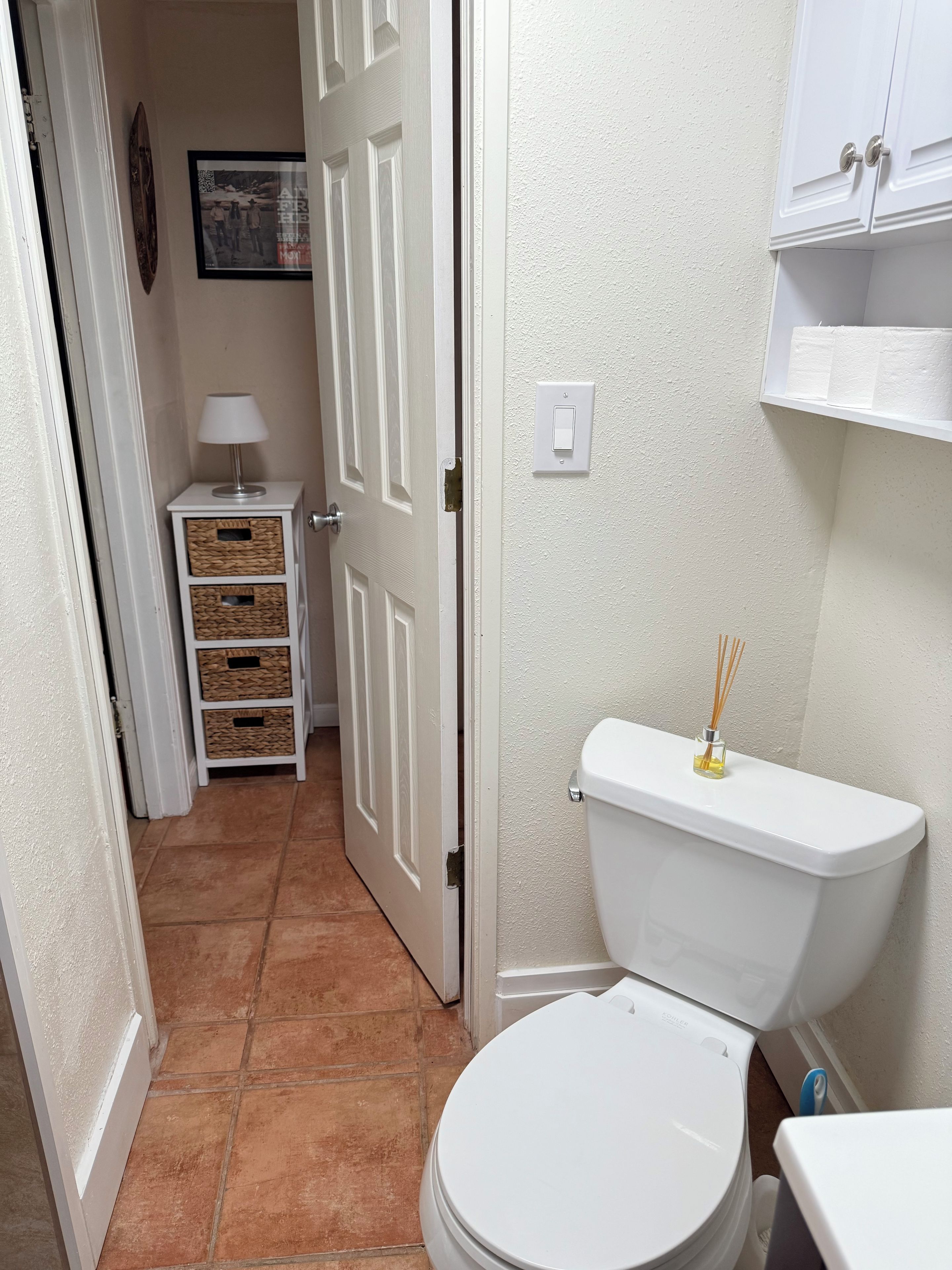 Een badkamer met een wit toilet, een klein schapje met een zakdoosje en een foto aan de muur.