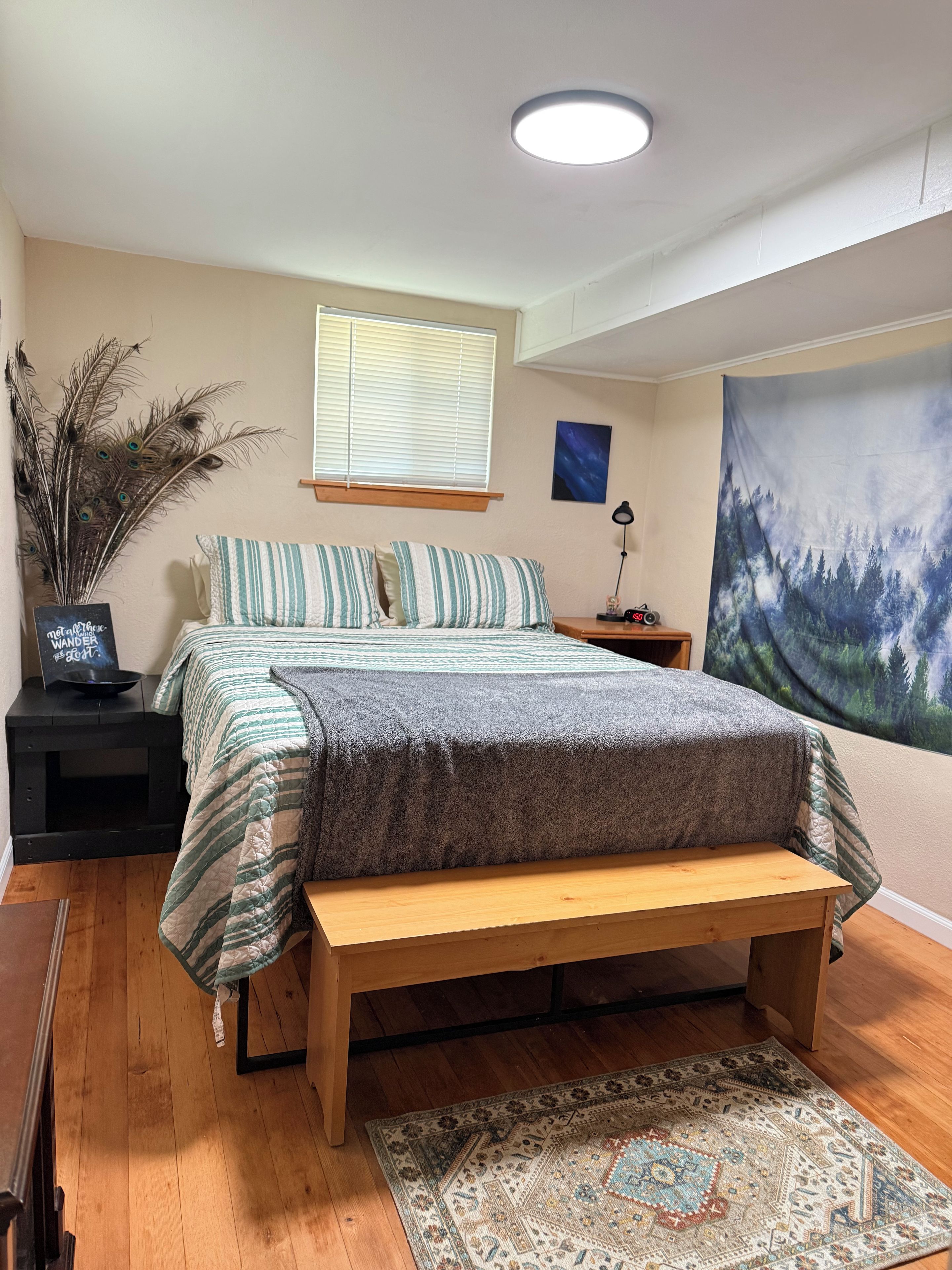 A bedroom with a bed, bedside table, lamp, and a large tapestry.