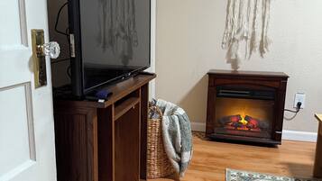 A living room with a television on a wooden stand, a fireplace with logs, a dreamcatcher on the wall, and a patterned rug on the floor.