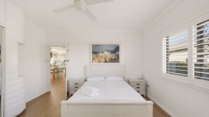 Ein Schlafzimmer mit einem Bett, Nachttischen, einem Deckenventilator, einem Fenster mit Jalousien und einem Bild an der Wand.