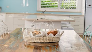 A wicker basket with seashells on a wooden table in a room with white cabinets and a window with blinds. - Rene's Cottage - a charming holiday rental nestled in the vibrant coastal town of Forster in NSW (Forster)