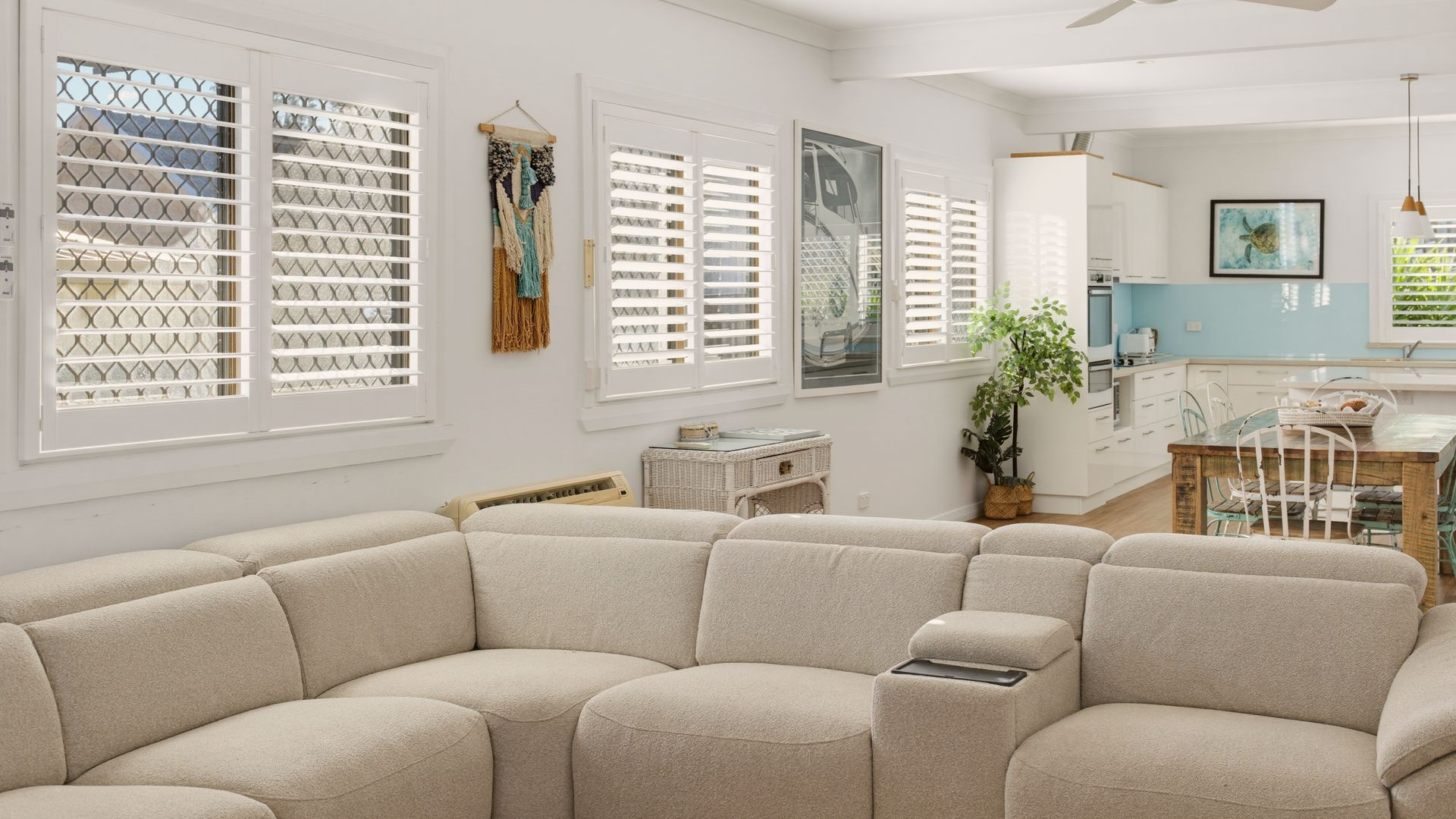 A living room with a sectional sofa, a dining area with a wooden table and chairs, and a kitchen in the background.