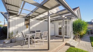 Ein überdachter Patio-Bereich mit Tisch und Stühlen, einem Kühlschrank und einem Blumentopf.