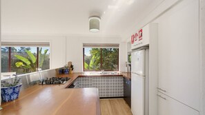 A modern kitchen with a central island, a built-in stove, and a refrigerator. - Jasmine Retreat, nestled in the serene coastal neighbourhood of Black Head in NSW (Black Head)