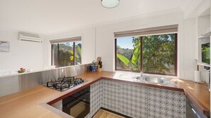 A kitchen with a gas stove, a sink, and large windows overlooking a garden. - Jasmine Retreat, nestled in the serene coastal neighbourhood of Black Head in NSW (Black Head)