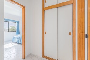 Ein Zimmer mit Schiebetür, einem Bett mit blauer Bettdecke und Blick auf einen Balkon mit blauem Vorhang.