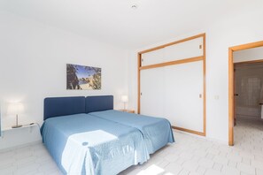 Un dormitorio con cama, mesita de noche, lámpara de noche, una puerta y un cuadro en la pared.