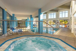 Un área de piscina interior con jacuzzi, sillas de descanso y vistas al exterior.