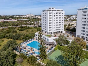 Ein Hochhaus-Hotel mit Schwimmbad, Tennisplatz und üppiger Bepflanzung.