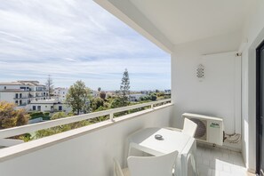 Un balcón con una mesa y sillas blancas, con vistas a una zona residencial con casas y árboles.
