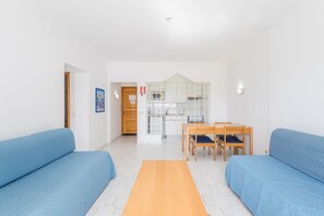 Ein modernes Wohnzimmer mit einer Couch, einem Esstisch mit Stühlen und einer Küchenzeile im Hintergrund.