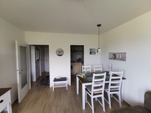A dining area with a table and chairs, a kitchen in the background, and a door leading to another room. - Hanseat Vacation Rental, Apartment 174, with an ocean view and dog-friendly. (Grömitz)