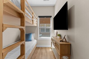 Ein Zimmer mit Etagenbetten, einem Fenster, einem Fernseher und einem Schreibtisch mit Schubladen.