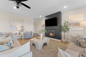 Ein modernes Wohnzimmer mit Kamin, bequemen Sitzmöglichkeiten und einem flachbildfernseher an der Wand.