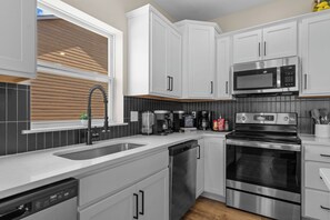 Eine moderne Küche mit weißen Schränken, Edelstahlgeräten, einem eingebauten Backofen und einer Kaffeemaschine.