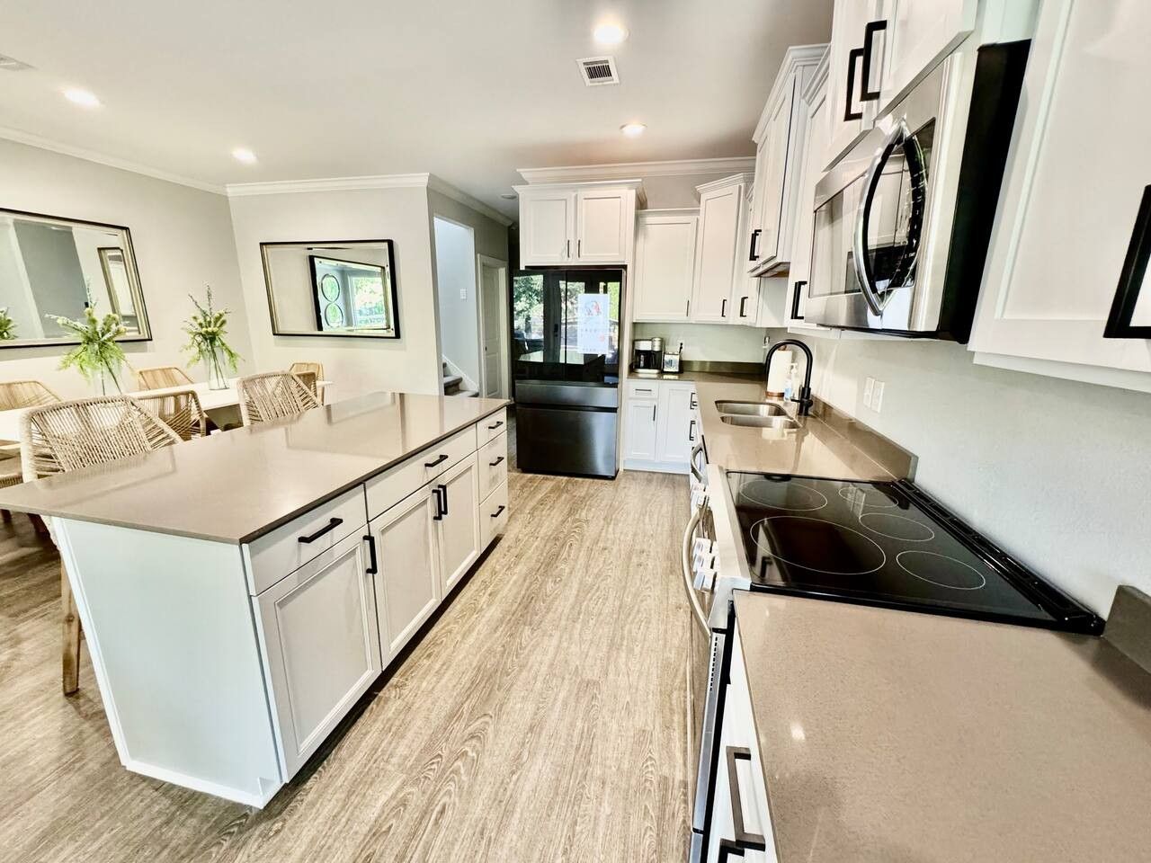 A modern kitchen with white cabinetry, a central island, and a black stovetop.
