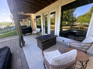 An outdoor patio with wicker furniture, a built-in fire pit, and a view of a pool and trees.