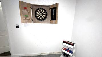 A dartboard mounted on a wall with a dartboard case and a small shelf with items.