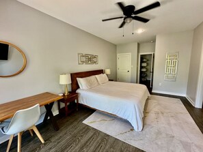 A bedroom with a bed, desk, chair, and a ceiling fan.