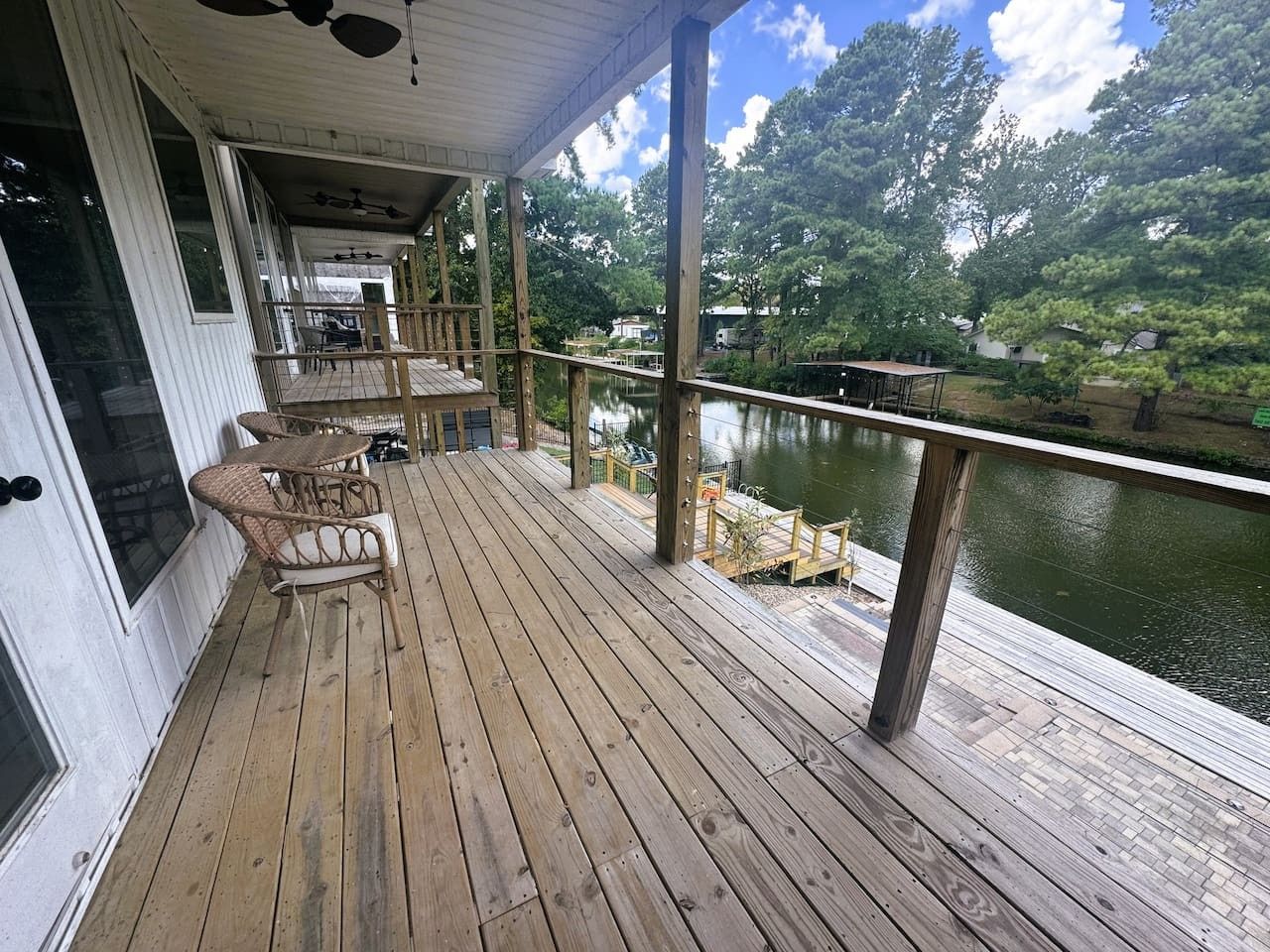 A wooden deck with outdoor furniture, overlooking a body of water and trees.