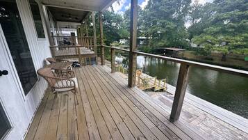 A wooden deck with outdoor furniture, overlooking a body of water and trees.