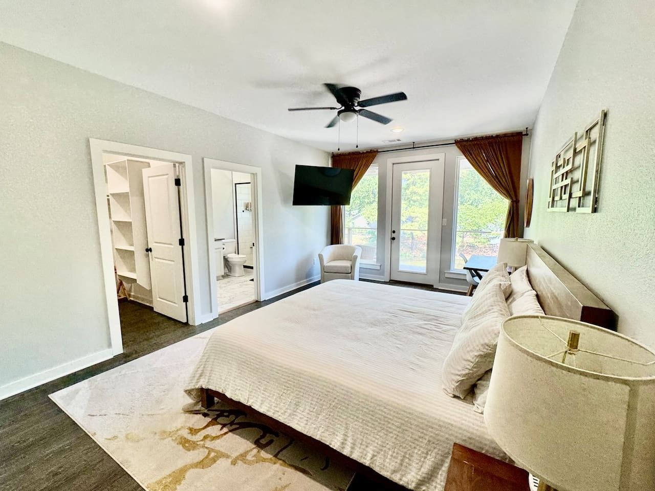 A bedroom with a bed, a ceiling fan, a TV, a chair, and a view of the outdoors.