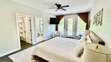 A bedroom with a bed, a ceiling fan, a TV, a chair, and a view of the outdoors.
