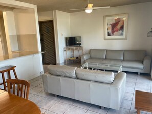 A living room with a sofa, a coffee table, a TV on a stand, and a dining area with chairs and a table. - 2 Bedroom Ocean-view Apartment (Gold Coast)