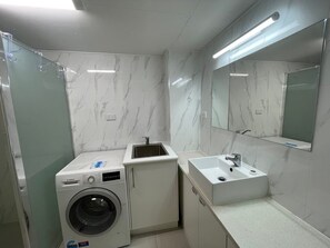 A compact bathroom with a washing machine, a sink, and a mirror. - 2 Bedroom Ocean-view Apartment (Gold Coast)