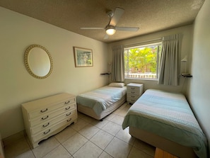 A bedroom with two beds, a dresser, a ceiling fan, a window with curtains, and a framed picture on the wall. - 2 Bedroom Ocean-view Apartment (Gold Coast)