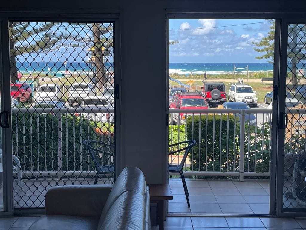A room with a view of the beach and parked cars through a glass door.