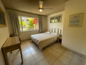 Une chambre à coucher avec un lit, un bureau, un ventilateur de plafond et une fenêtre avec des rideaux.