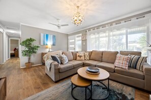Ein geräumiges Wohnzimmer mit einer großen Eckcouch, einem runden Couchtisch und einer Topfpflanze.