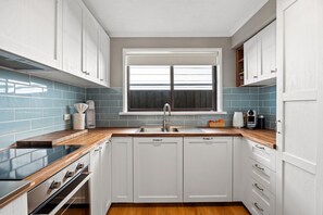 Eine moderne Küche mit weißen Schränken, einer Holzausziehtafel, einem eingebauten Backofen und einem Fenster über der Spüle.