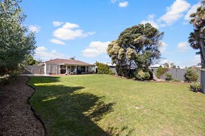 Un jardin à l’arrière d’une maison, avec une maison, un patio couvert et un grand arbre.