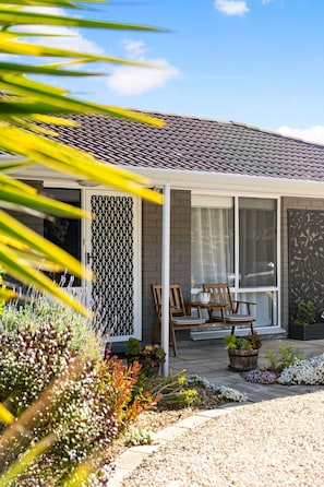 A house with a tiled roof, a covered porch with chairs, and a garden with various plants. - Hazel Haven—Beach Lifestyle with Spacious Garden (Goolwa Beach)