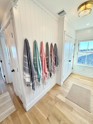 A hallway with a row of towels hanging on the wall, wooden flooring, and a view through a window.