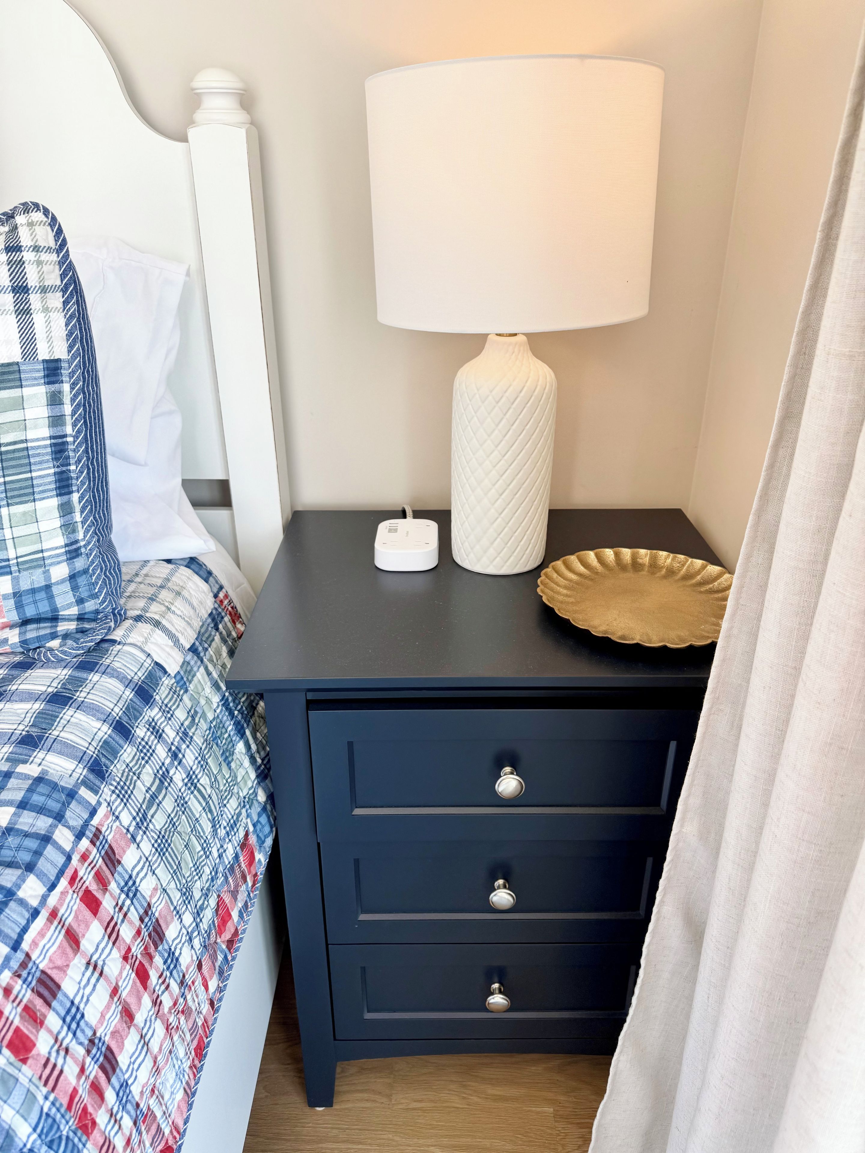 A bedroom with a bed, a bedside table with a lamp, and a nightstand with drawers.