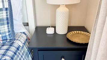A bedroom with a bed, a bedside table with a lamp, and a nightstand with drawers.