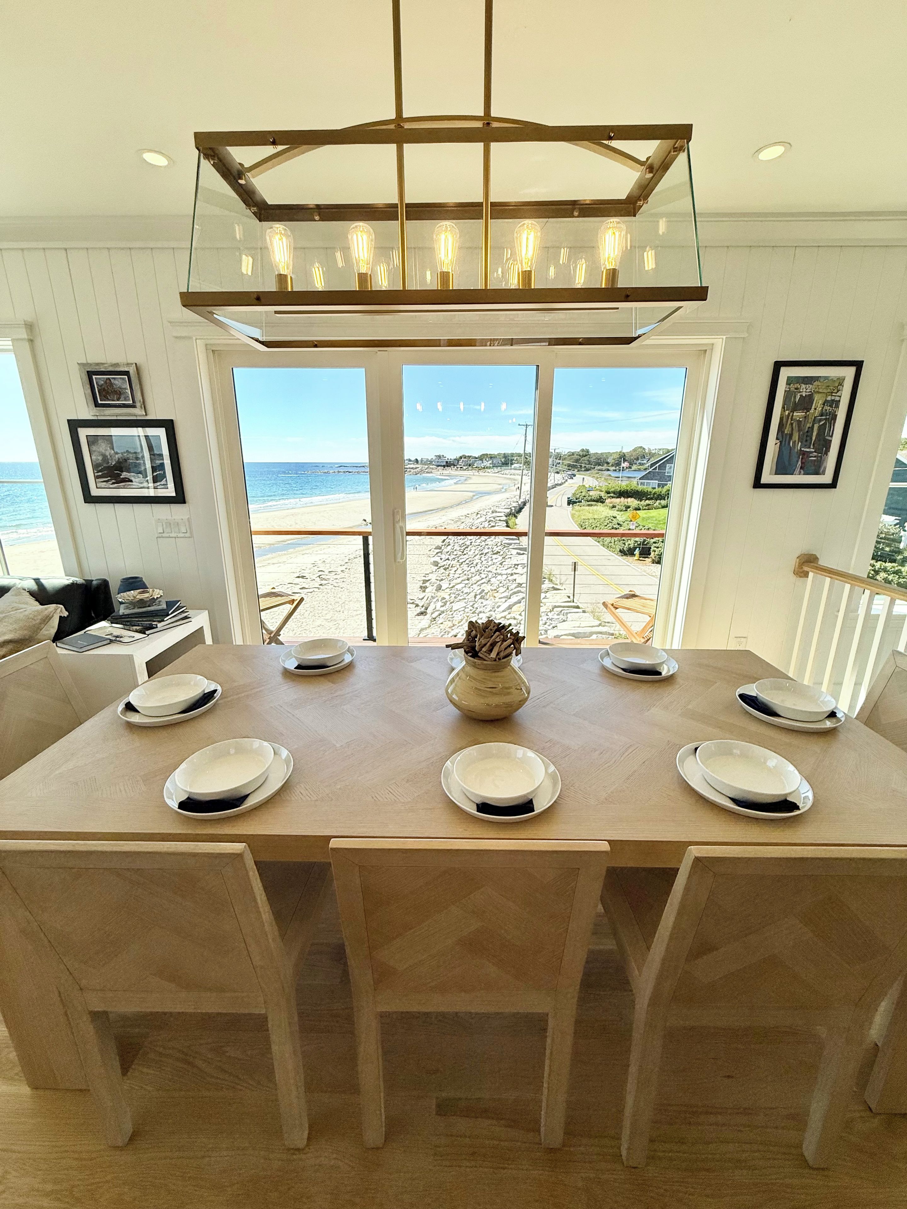 A dining area with a large table, chairs, and a view of the beach.