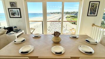 A dining area with a large table, chairs, and a view of the beach.