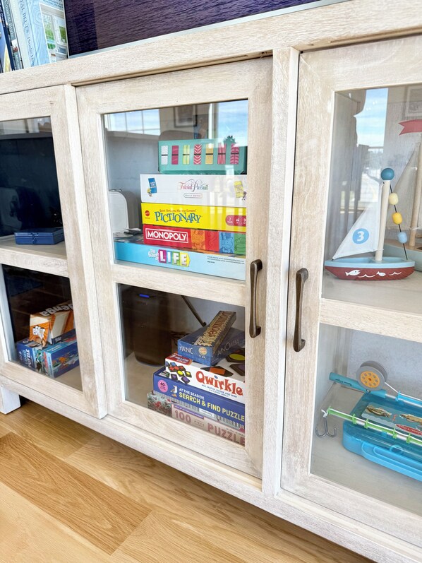 A wooden cabinet with glass doors containing various board games and puzzles.