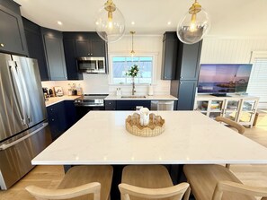 A modern kitchen with dark cabinets, stainless steel appliances, a large island with seating, and pendant lighting.