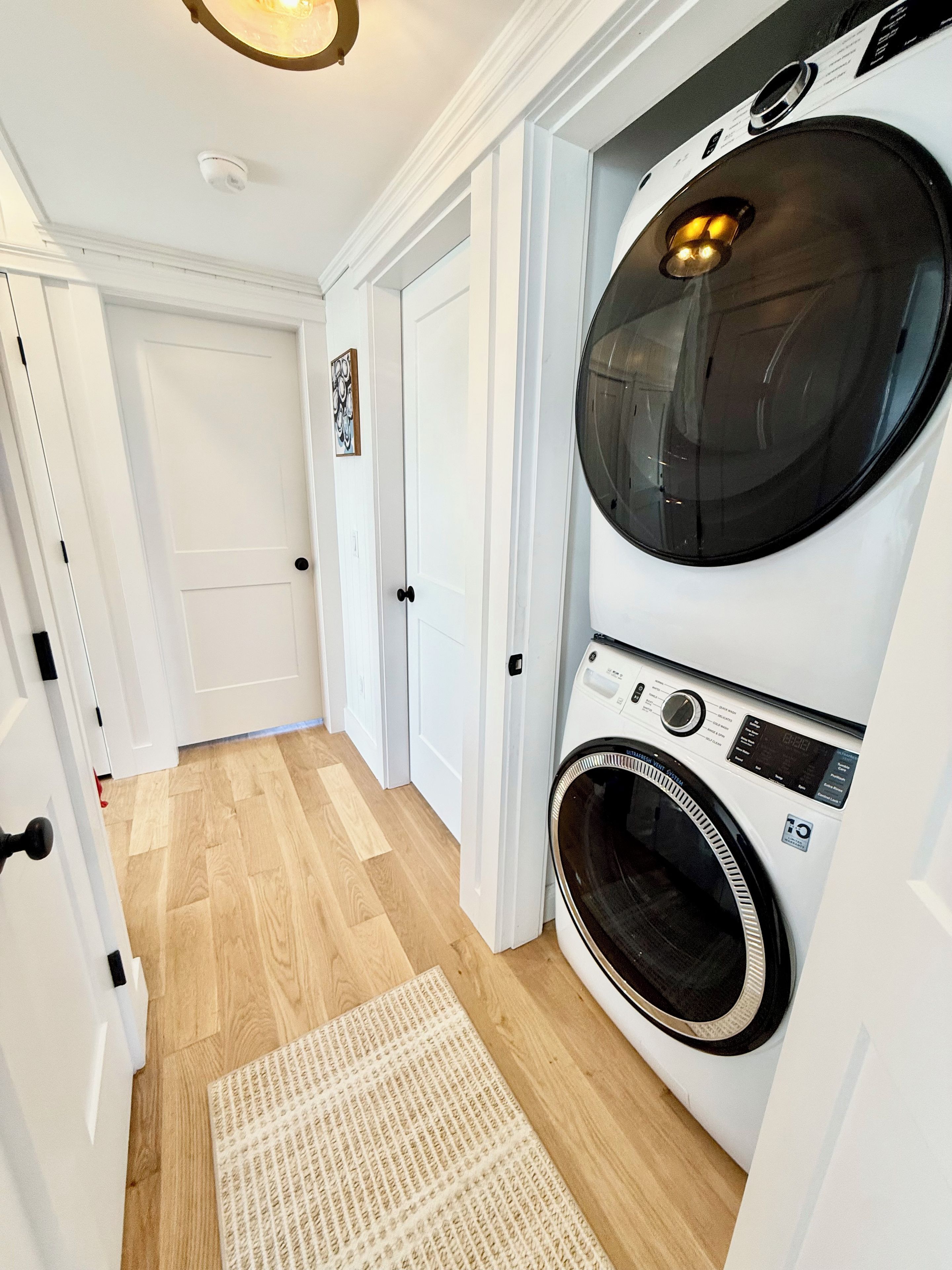 A laundry room with a front-loading washer and dryer, wooden flooring, and a white door.