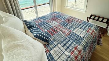 A bedroom with a bed, two windows, a view of the beach, and a wooden headboard.